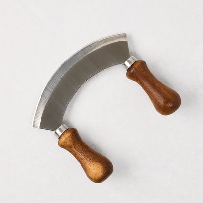 Mezzaluna blade with a curved stainless steel blade and two light brown wooden handles.