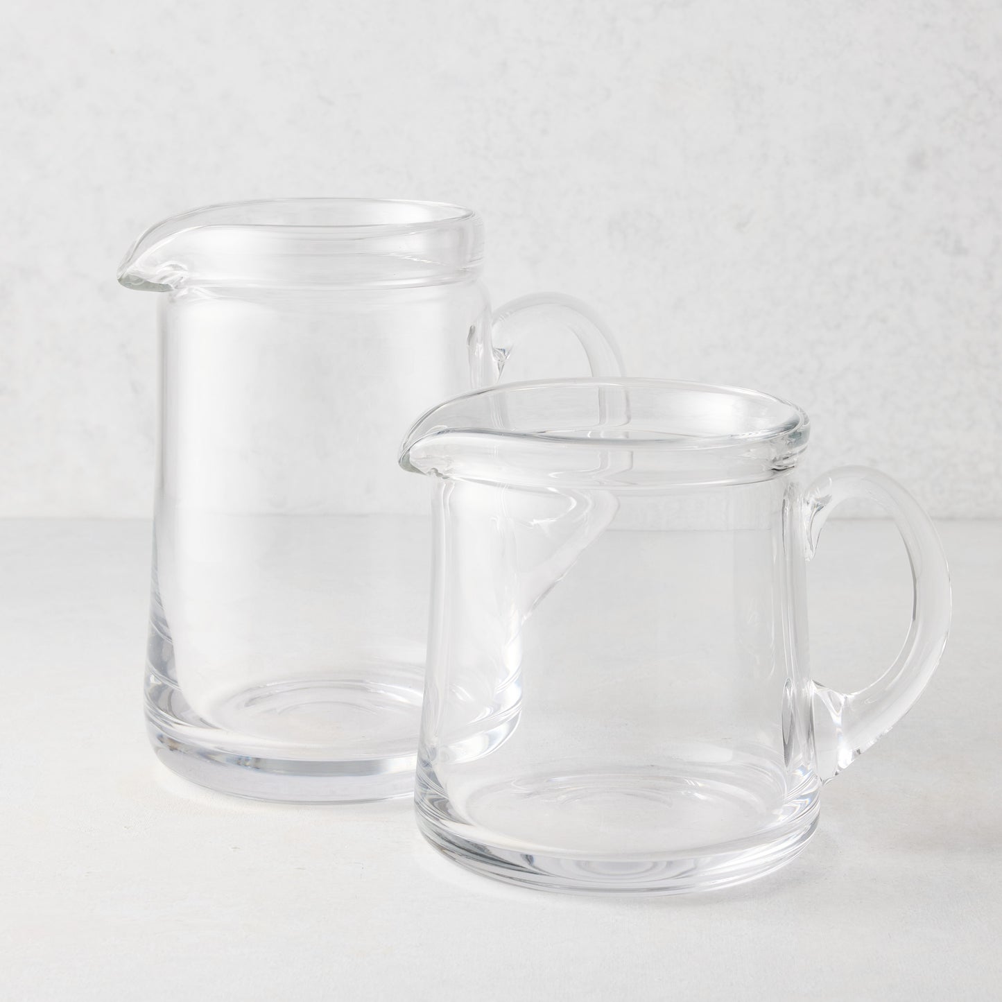 Two clear glass Oxford pitchers, one large and one small, with hand-molded rims and handles.