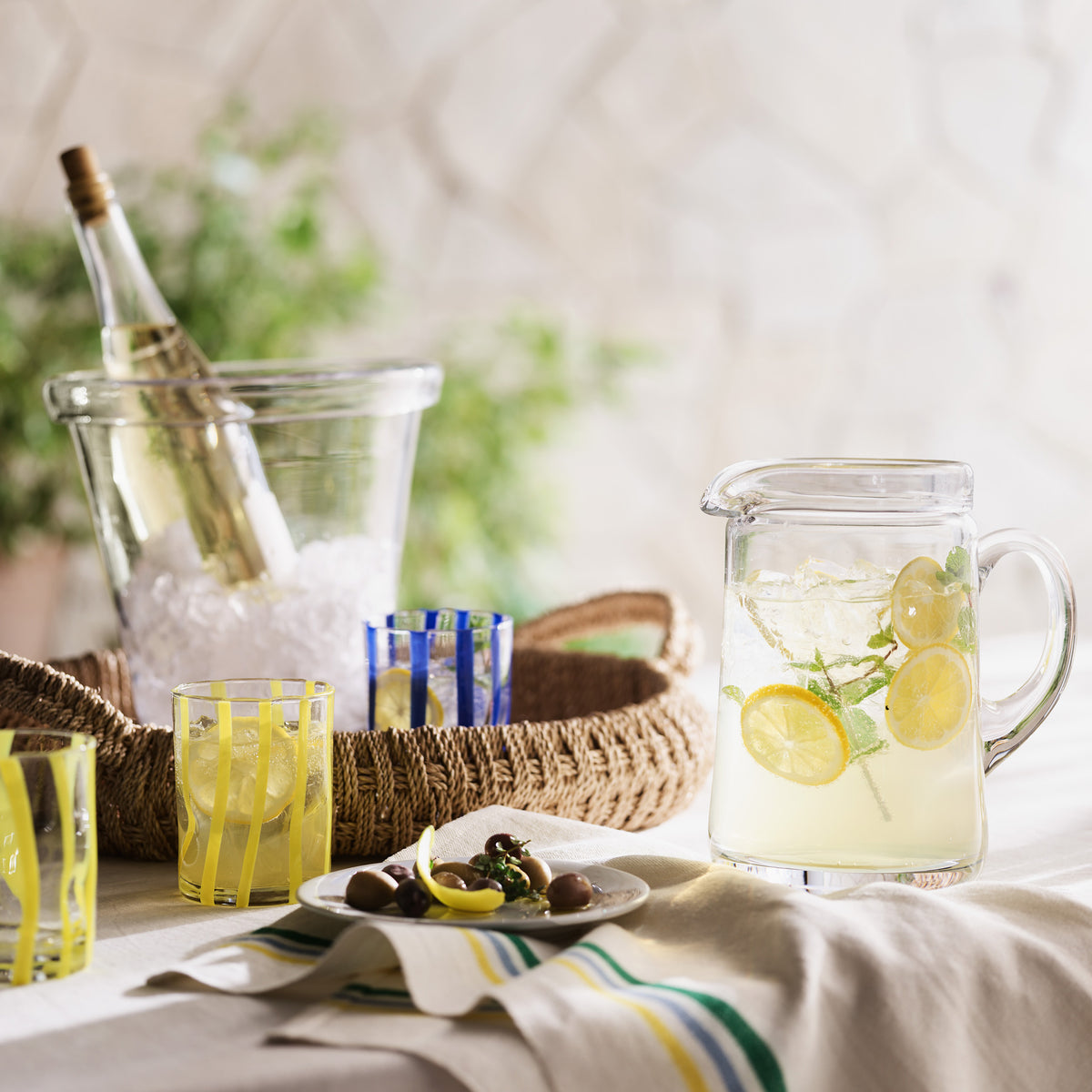Large Oxford glass pitcher with hand-molded rim, filled with lemonade, on a table with drinks and snacks.