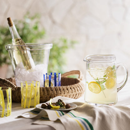 Large Oxford glass pitcher with hand-molded rim, filled with lemonade, on a table with drinks and snacks.