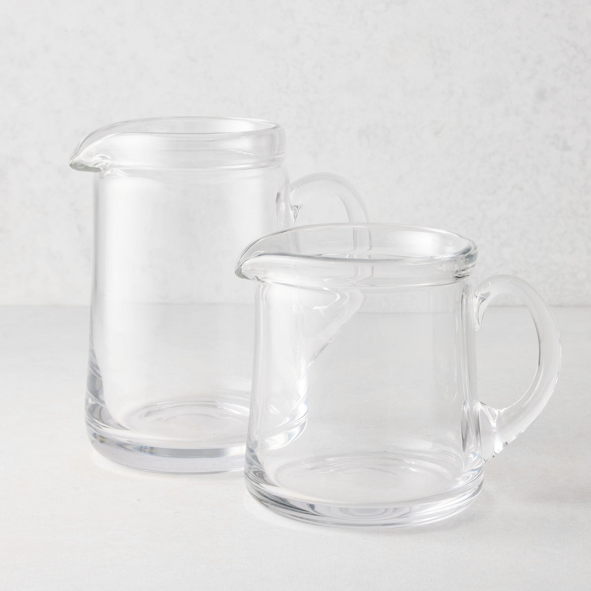 Two clear glass Oxford pitchers, one large and one small, with hand-molded rims and handles.