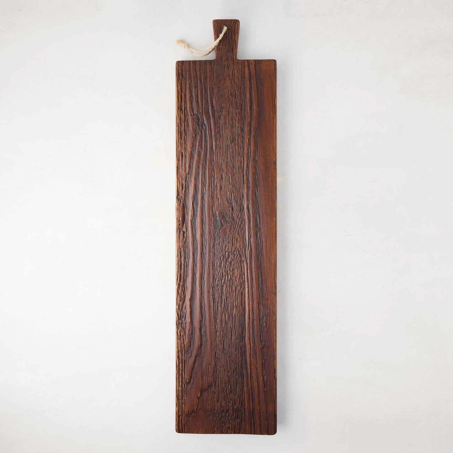 Long, dark brown European pine serving plank with a handle and rope hanger, showcasing unique wood grain.