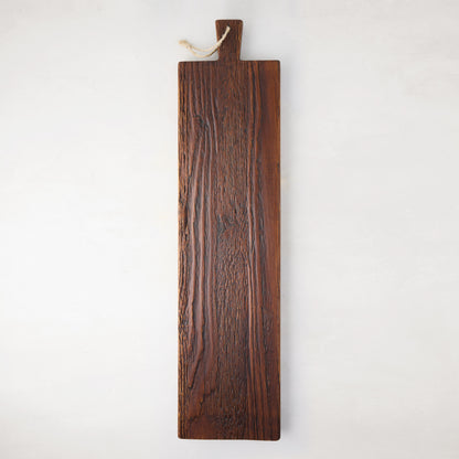 Long, dark brown European pine serving plank with a handle and rope hanger, showcasing unique wood grain.