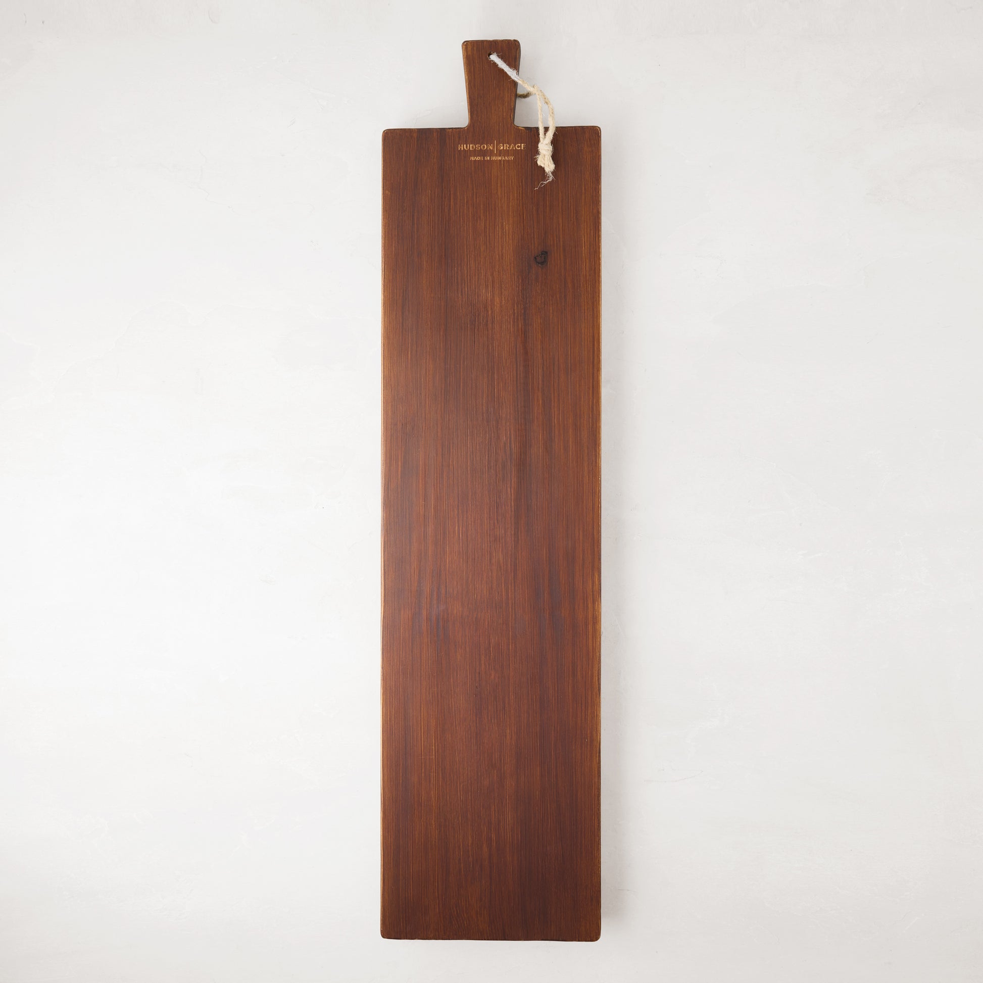Long, dark brown European pine serving plank with a handle and rope for hanging.