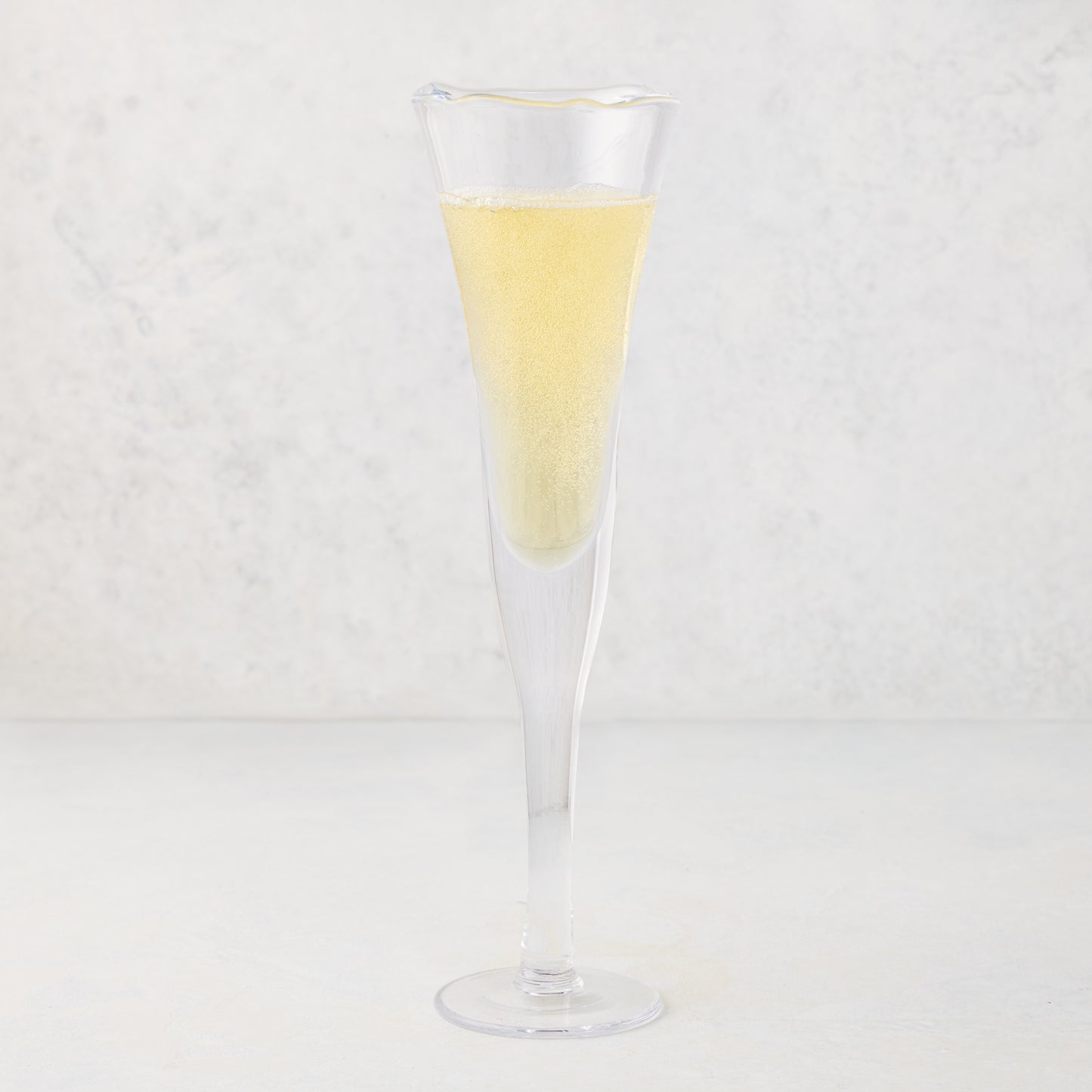 Clear, thick, air-blown glass champagne flute with a rippled rim, filled with sparkling yellow liquid.