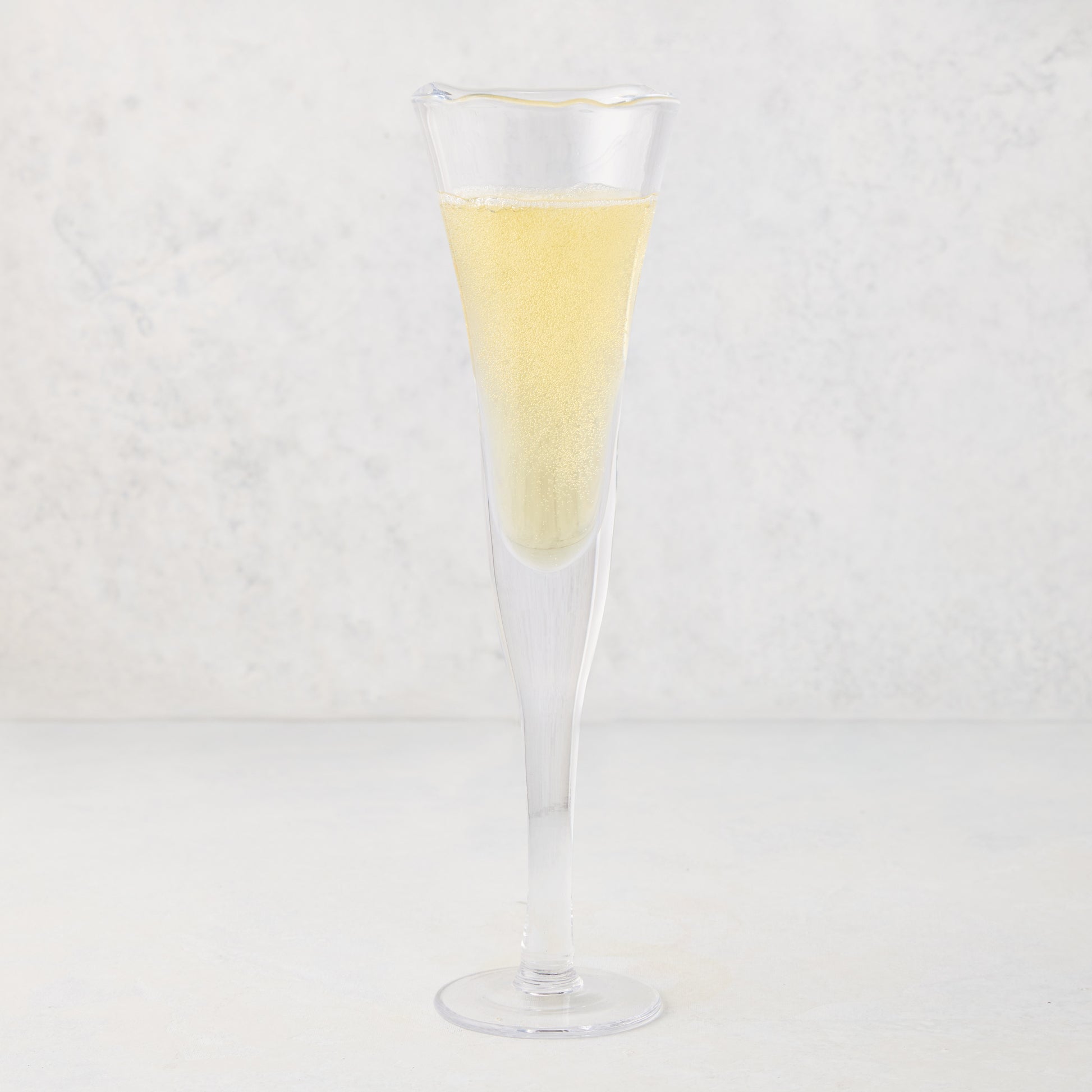 Clear, thick, air-blown glass champagne flute with a rippled rim, filled with sparkling yellow liquid.