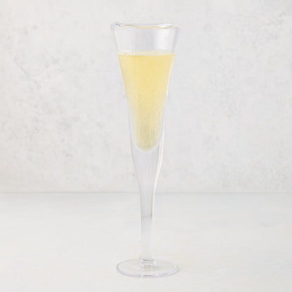 Clear, thick, air-blown glass champagne flute with a rippled rim, filled with sparkling yellow liquid.