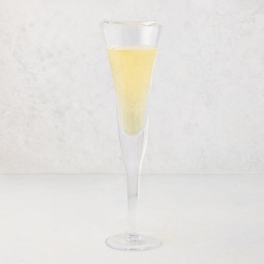 Clear, thick, air-blown glass champagne flute with a rippled rim, filled with sparkling yellow liquid.