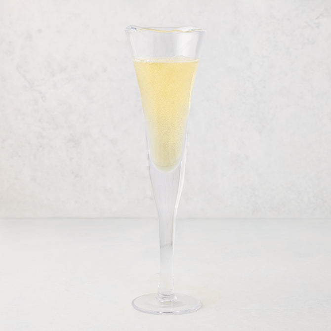 Clear, thick, air-blown glass champagne flute with a rippled rim, filled with sparkling yellow liquid.