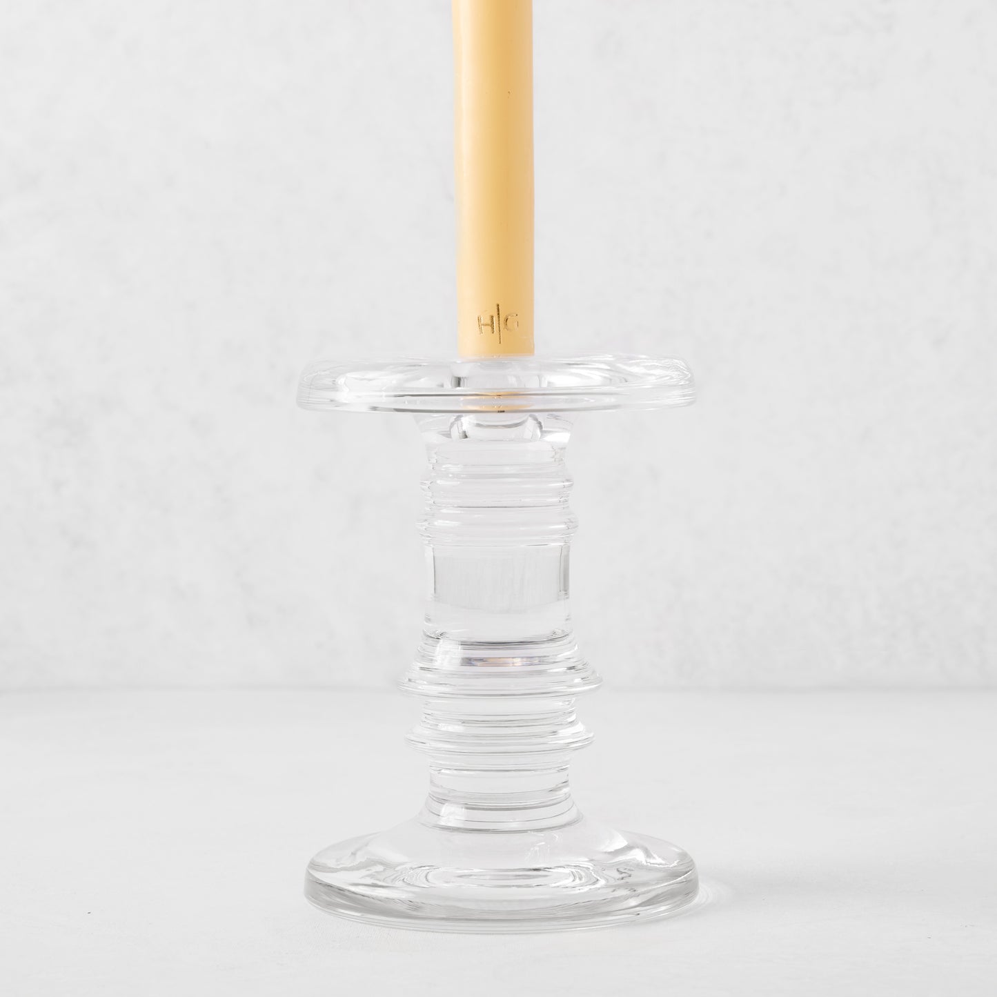 Clear glass taper candleholder with ridged design, holding a cream candle.