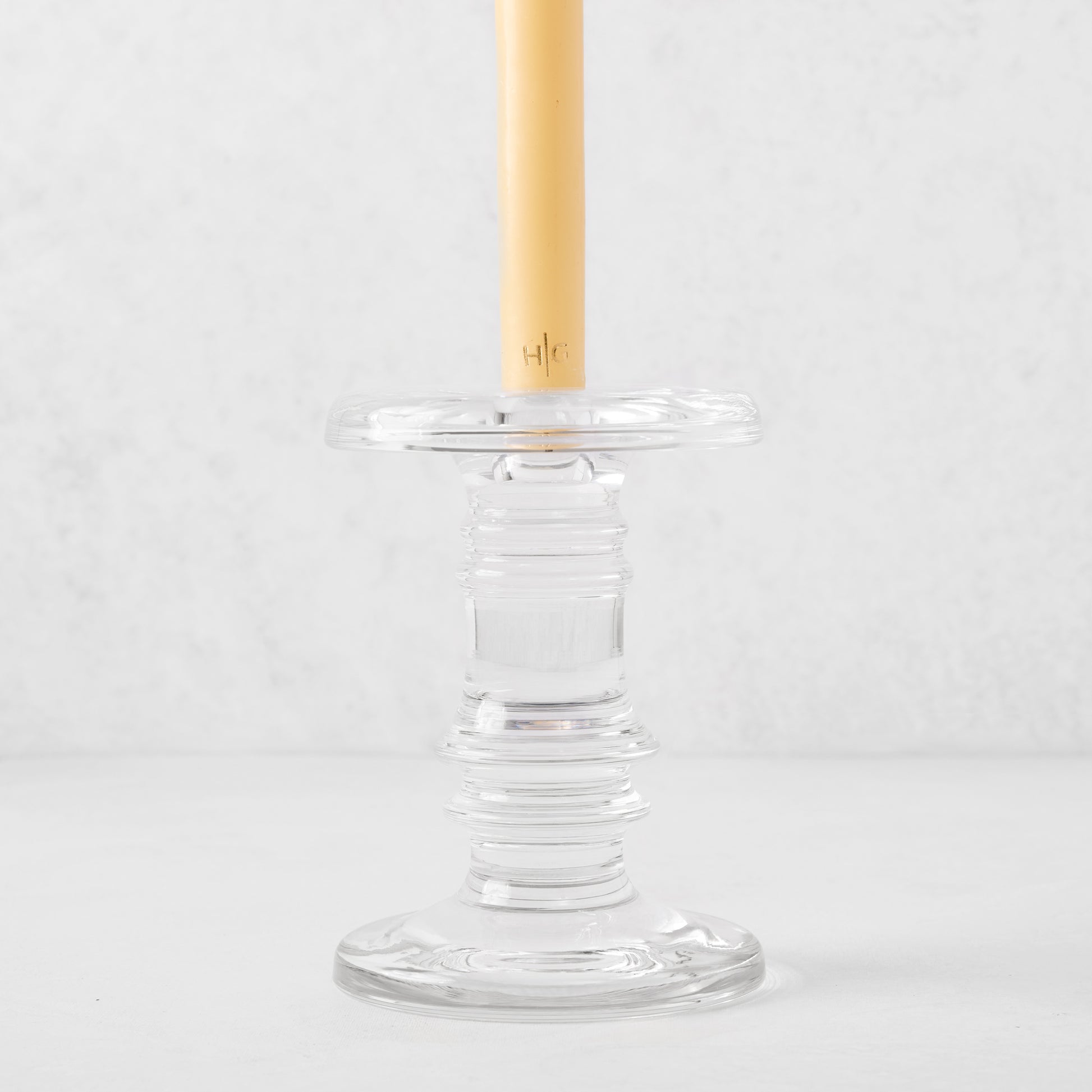 Clear glass taper candleholder with ridged design, holding a cream candle.