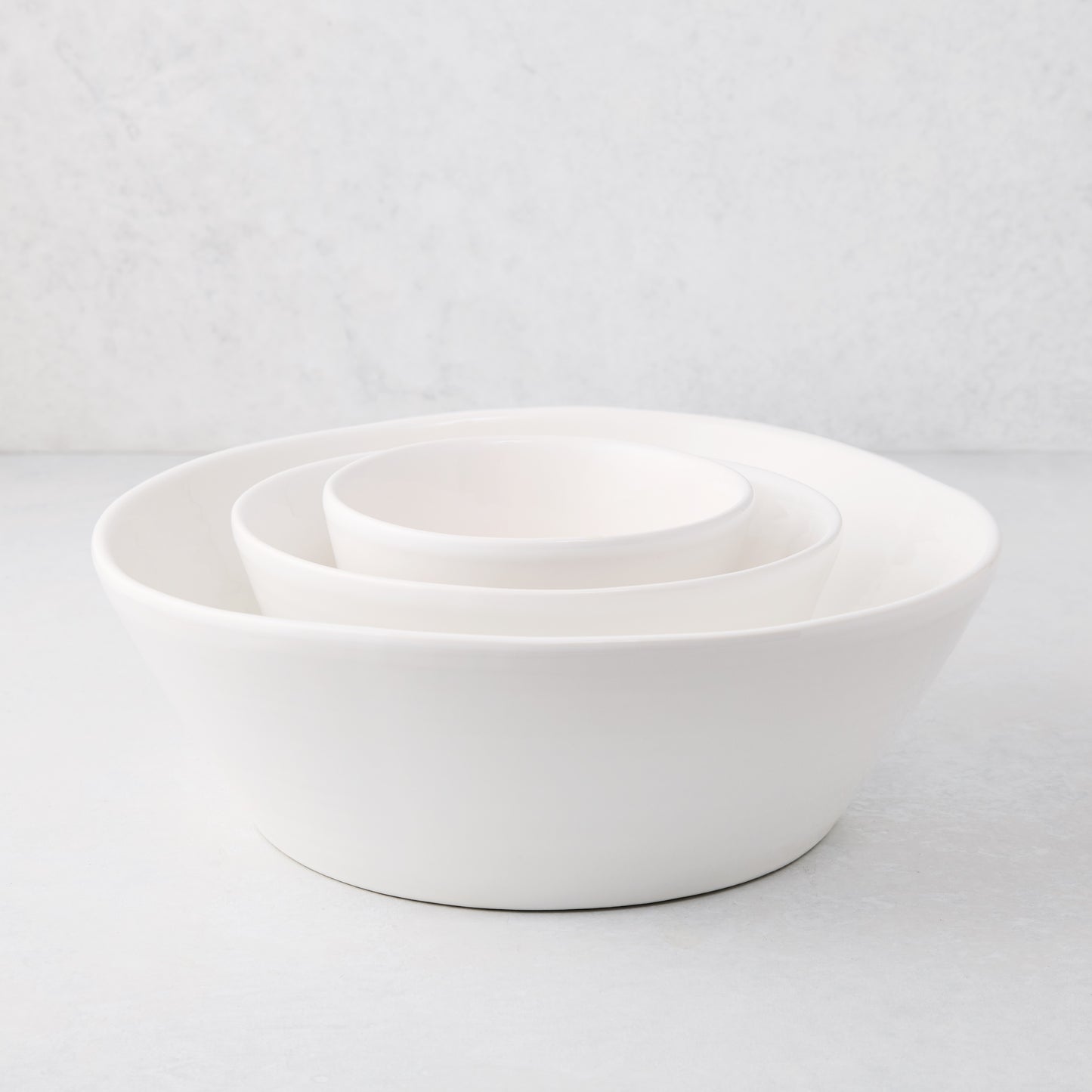 Set of three white spiral ceramic serve bowls, handmade in Portugal, nested on a light background.