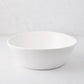 Large white spiral ceramic serve bowl with high edges on a light background.