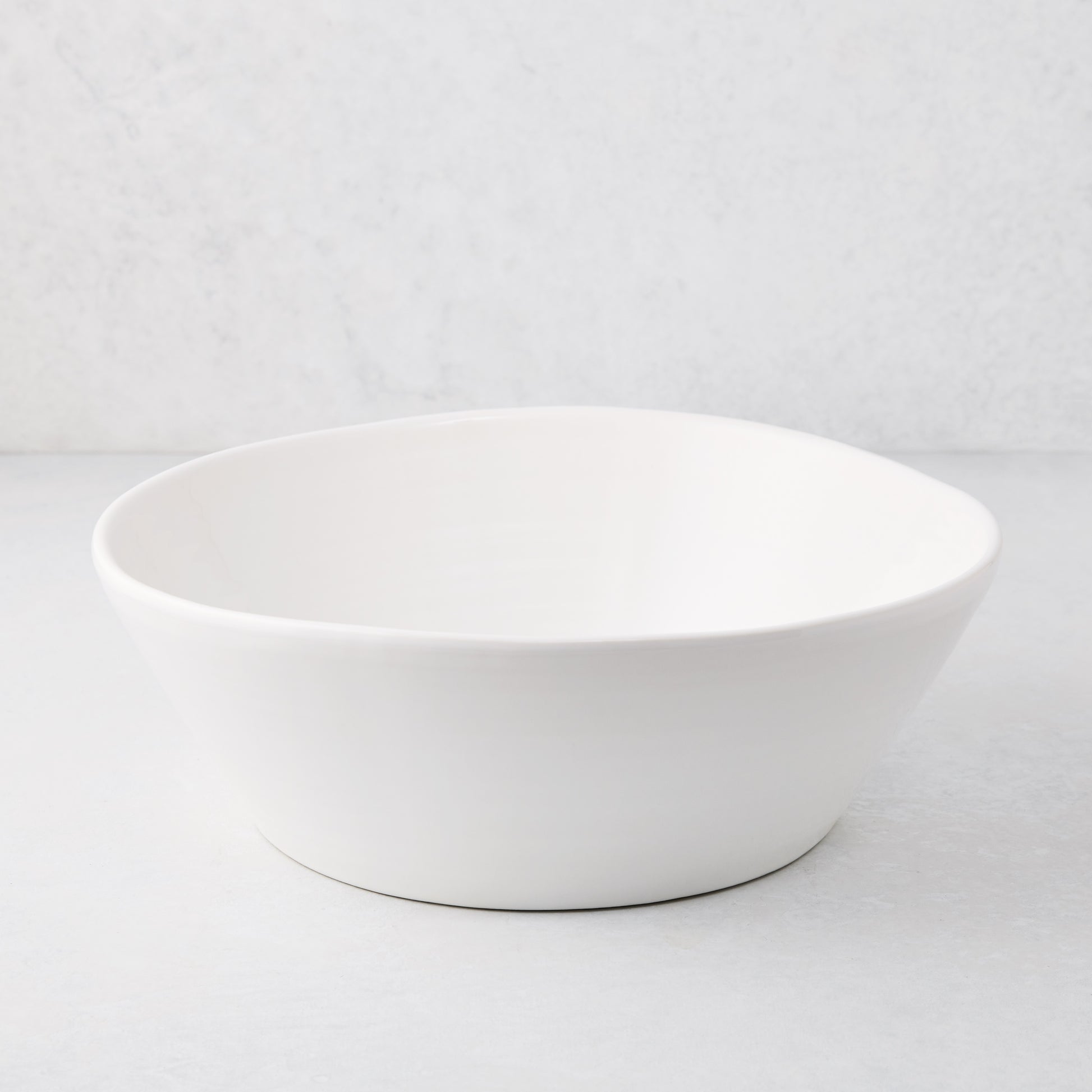 Large white spiral ceramic serve bowl with high edges on a light background.