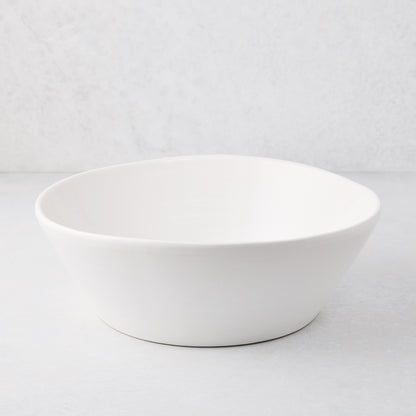 Large white spiral ceramic serve bowl with high edges on a light background.