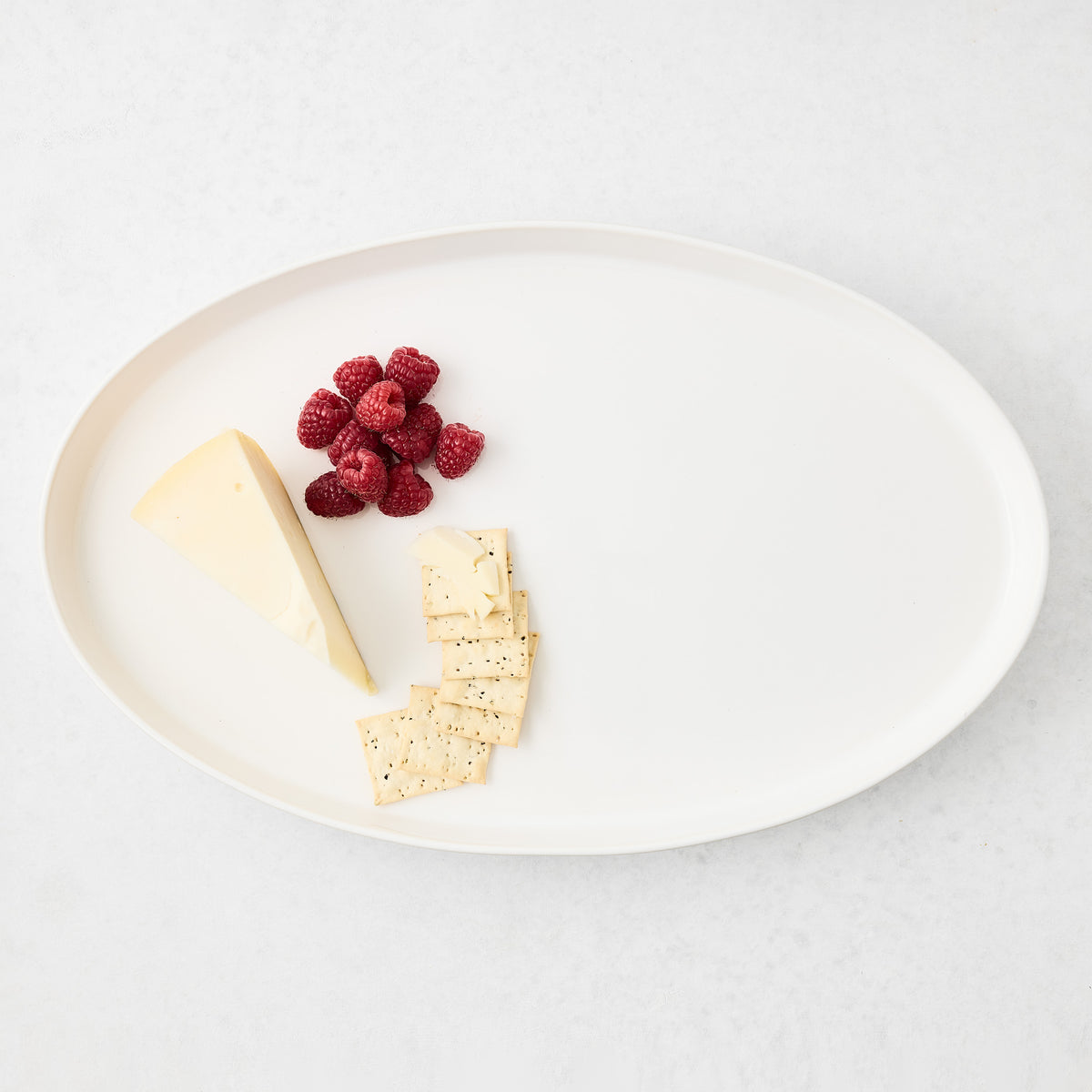 Large white oval stoneware serving platter topped with cheese, crackers, and fresh raspberries.