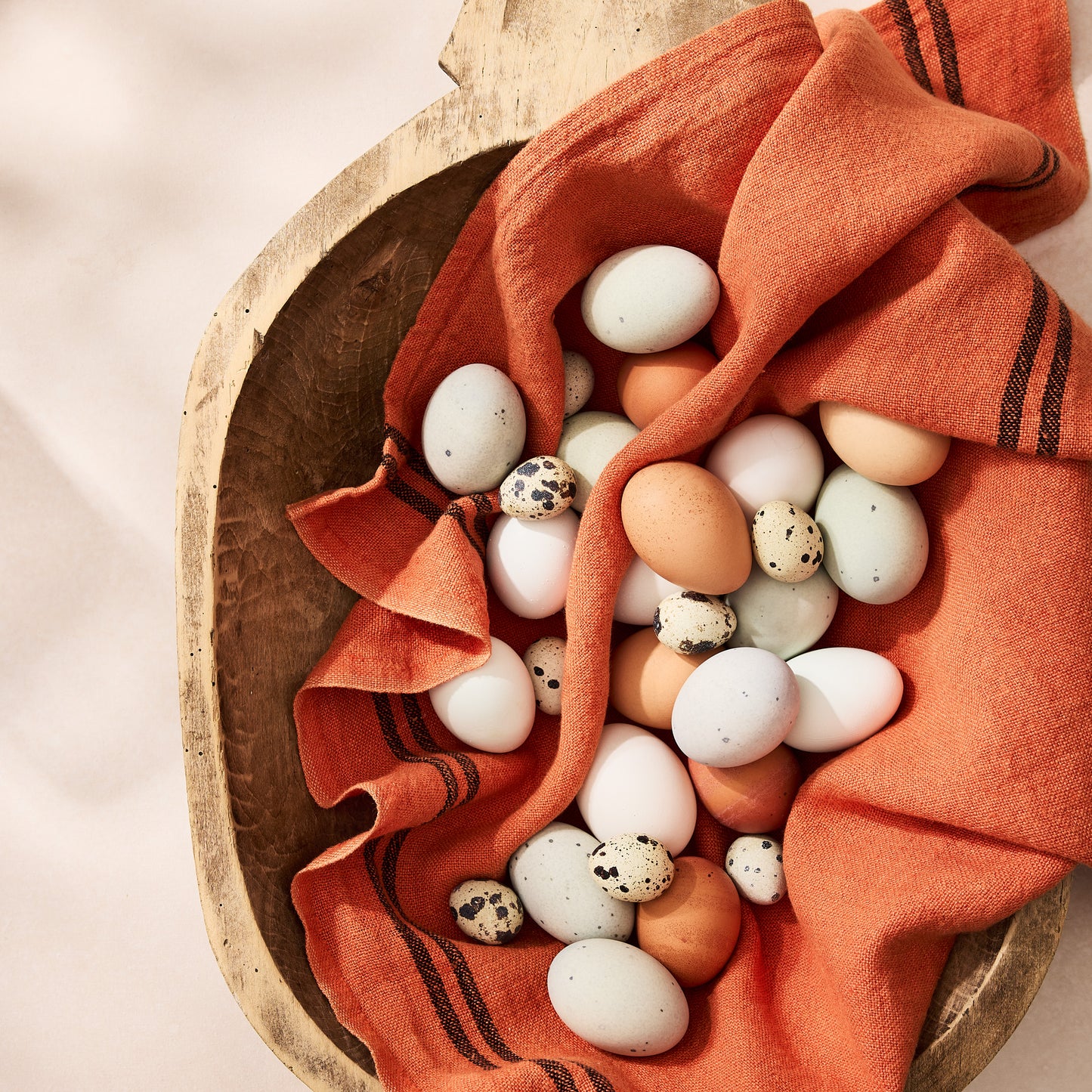 Large vintage reclaimed wood bowl with an orange linen and assorted eggs.