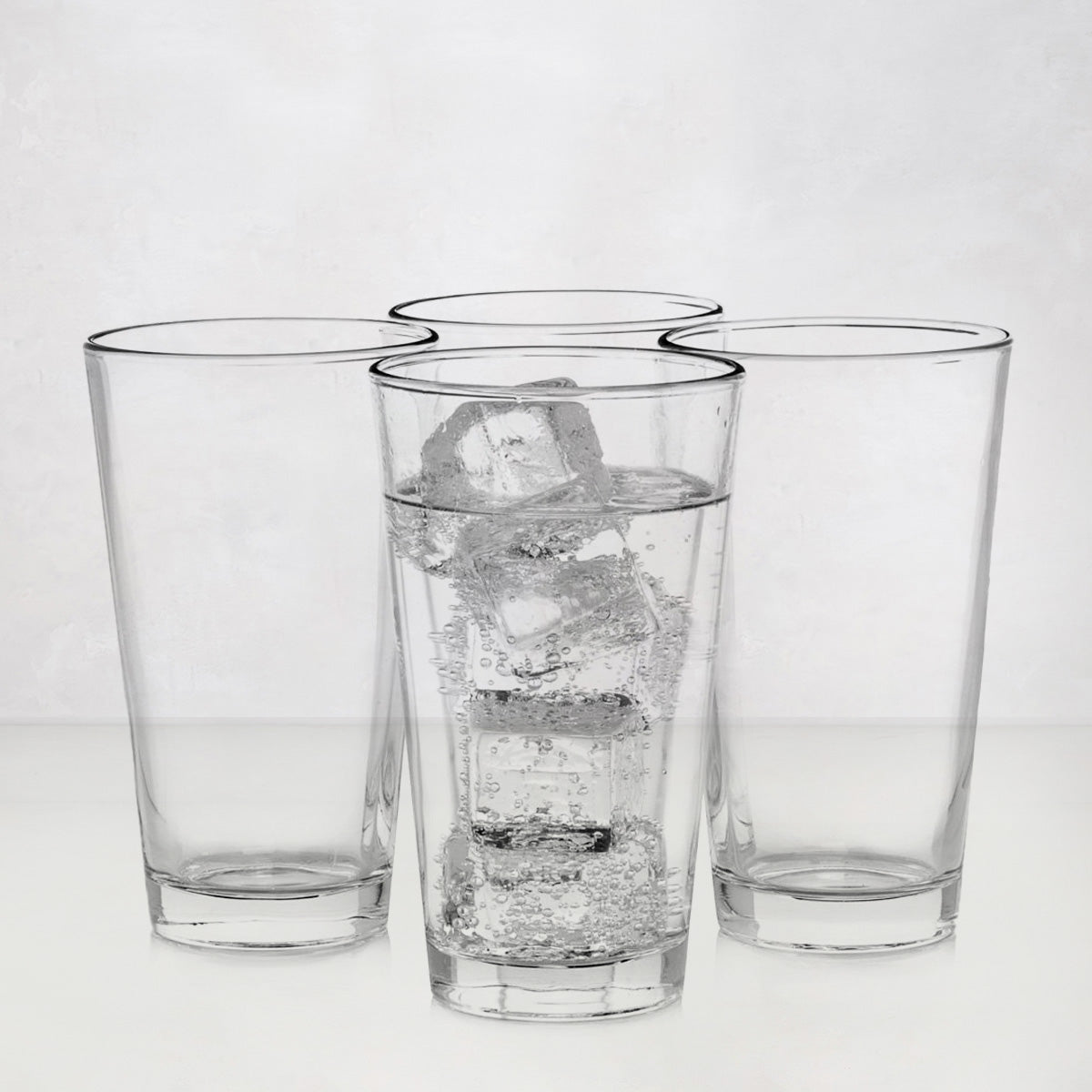 Four clear, tall Hudson Grace drinking glasses; one filled with water and ice.
