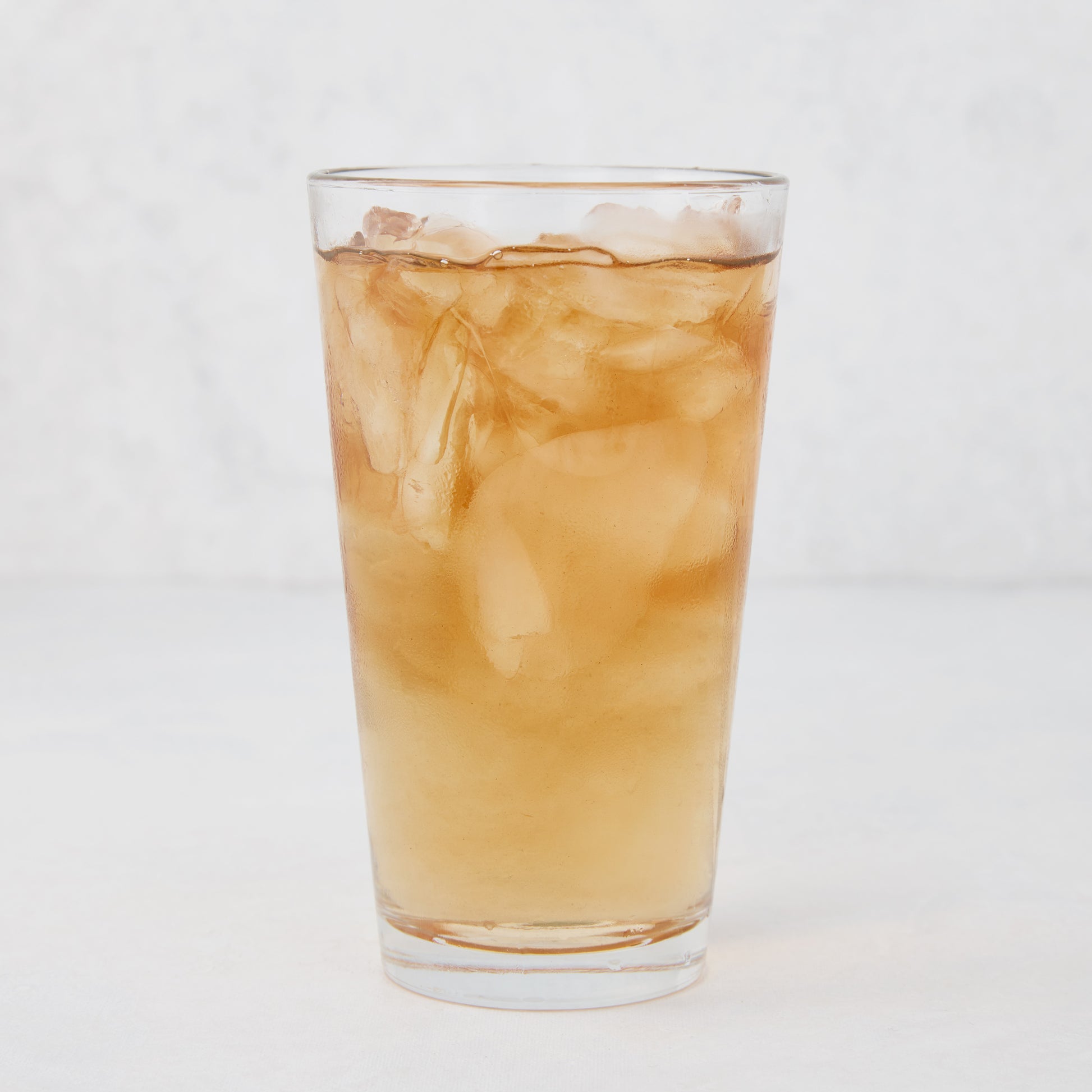Tall, clear Hudson Grace glass filled with ice and a brown beverage.