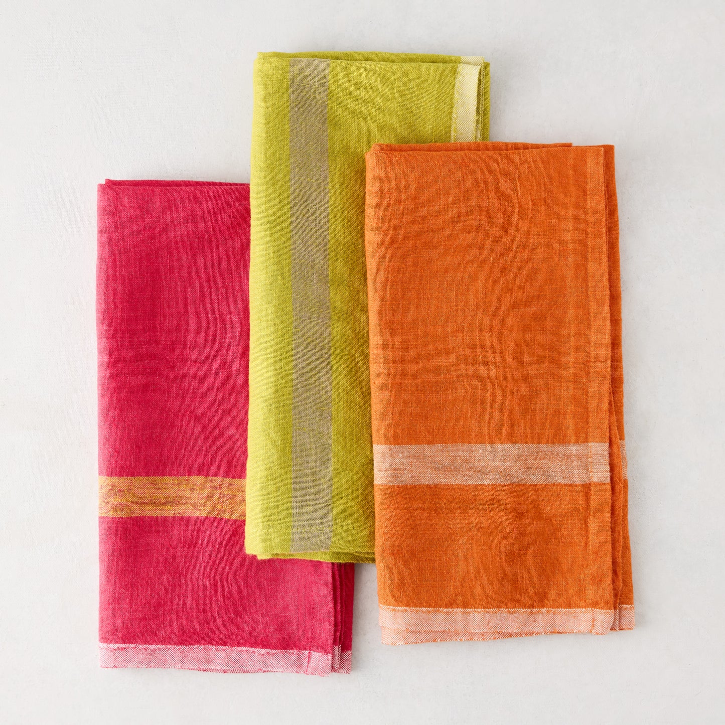 Folded bright orange, lime, and pink laundered linen napkins with paler stripes.