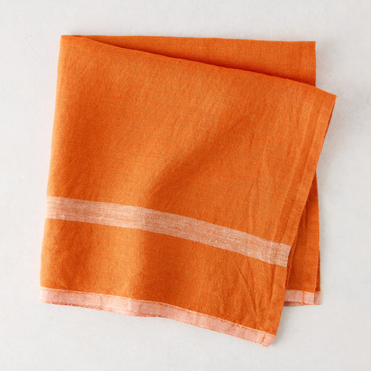 Laundered bright orange linen napkin, 22" square, with paler horizontal stripes.