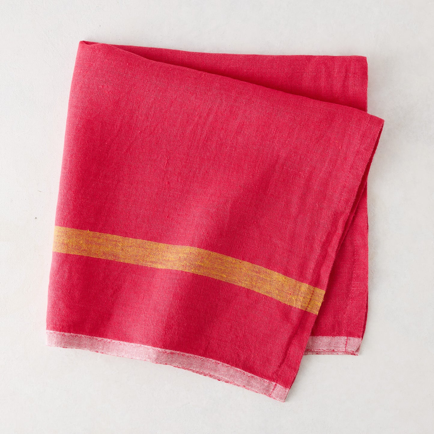 Folded bright pink linen napkin with a golden stripe and paler edges.