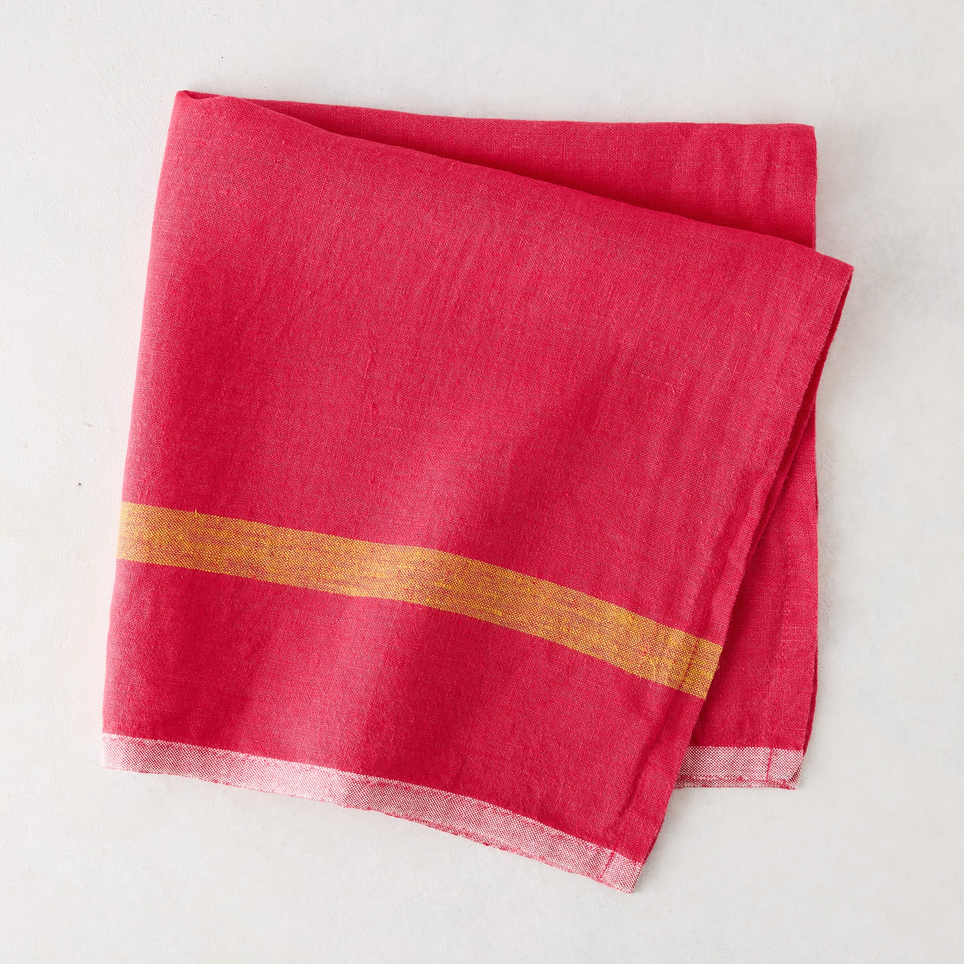 Folded bright pink linen napkin with a golden stripe and paler edges.