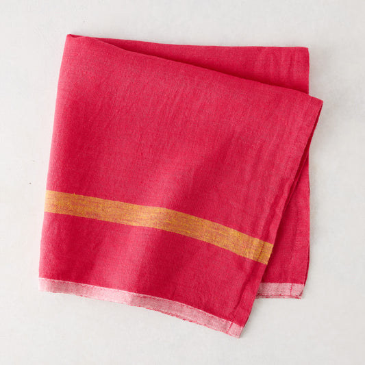 Folded bright pink linen napkin with a golden stripe and paler edges.