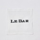 White linen cocktail napkin coaster with "LE BAR" hand-embroidered in black.