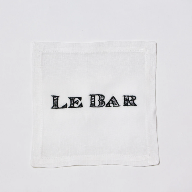 White linen cocktail napkin coaster with "LE BAR" hand-embroidered in black.