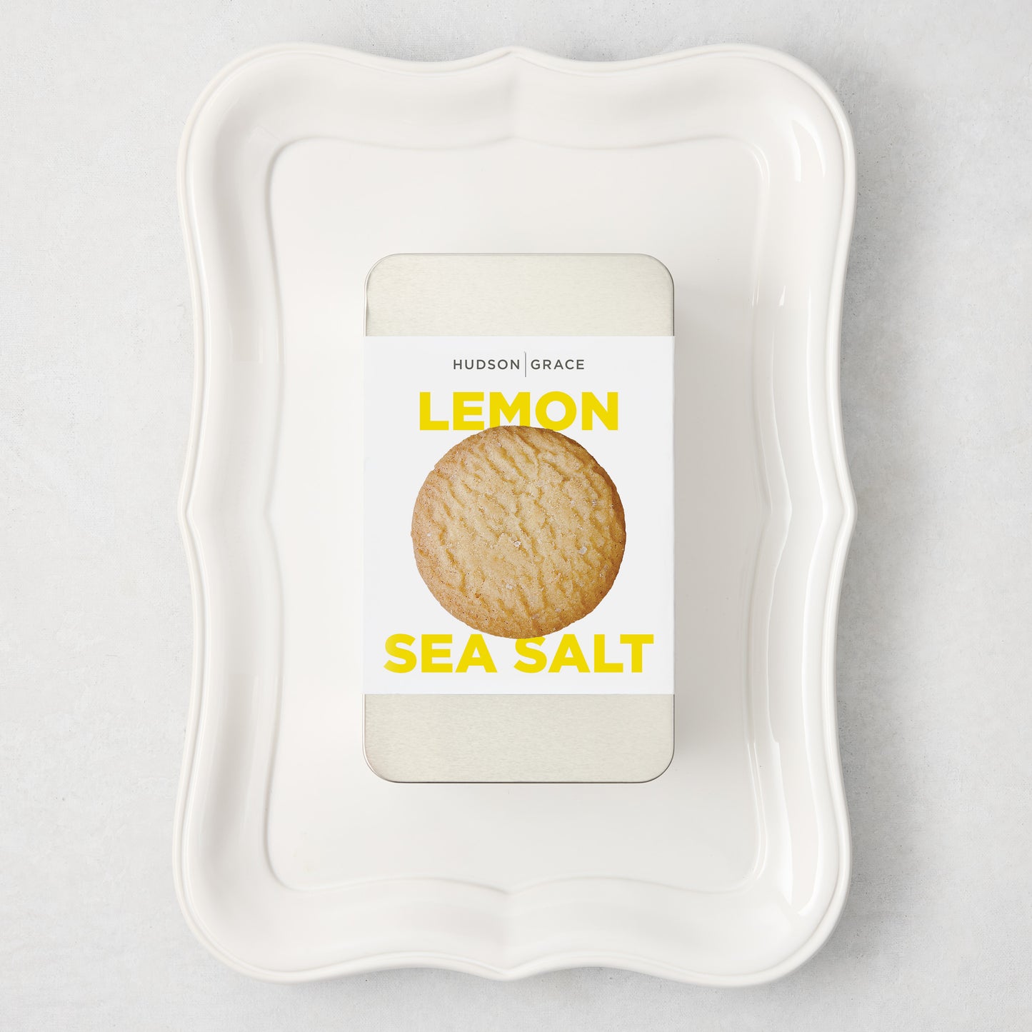 White rectangular Colette Platter with curved edges, holding a silver tin of Hudson Grace Lemon Sea Salt cookies.