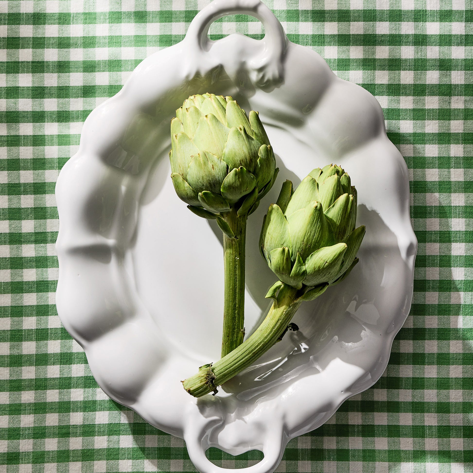White ceramic oval serving platter with handles, 18" long, on a green gingham tablecloth.