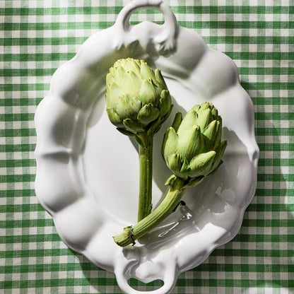 White ceramic oval serving platter with handles, 18" long, on a green gingham tablecloth.