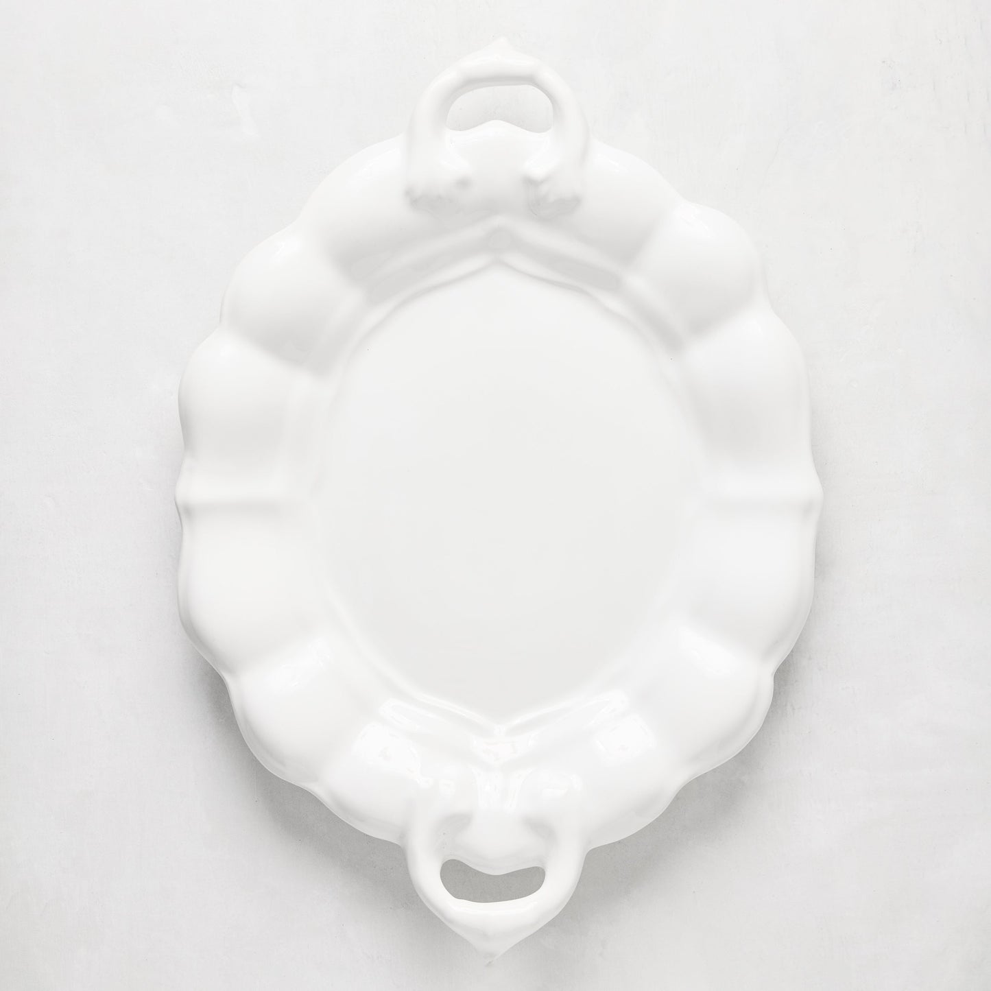 White oval ceramic serving platter with scalloped edges and handles.