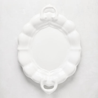 White oval ceramic serving platter with scalloped edges and handles.