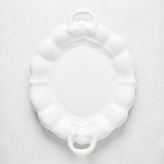 White oval ceramic serving platter with scalloped edges and handles.