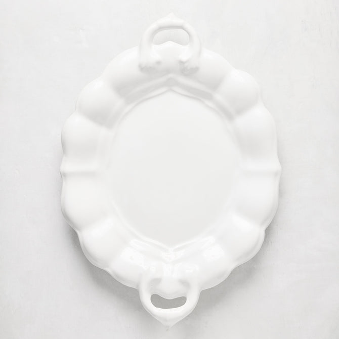 White oval ceramic serving platter with scalloped edges and handles.