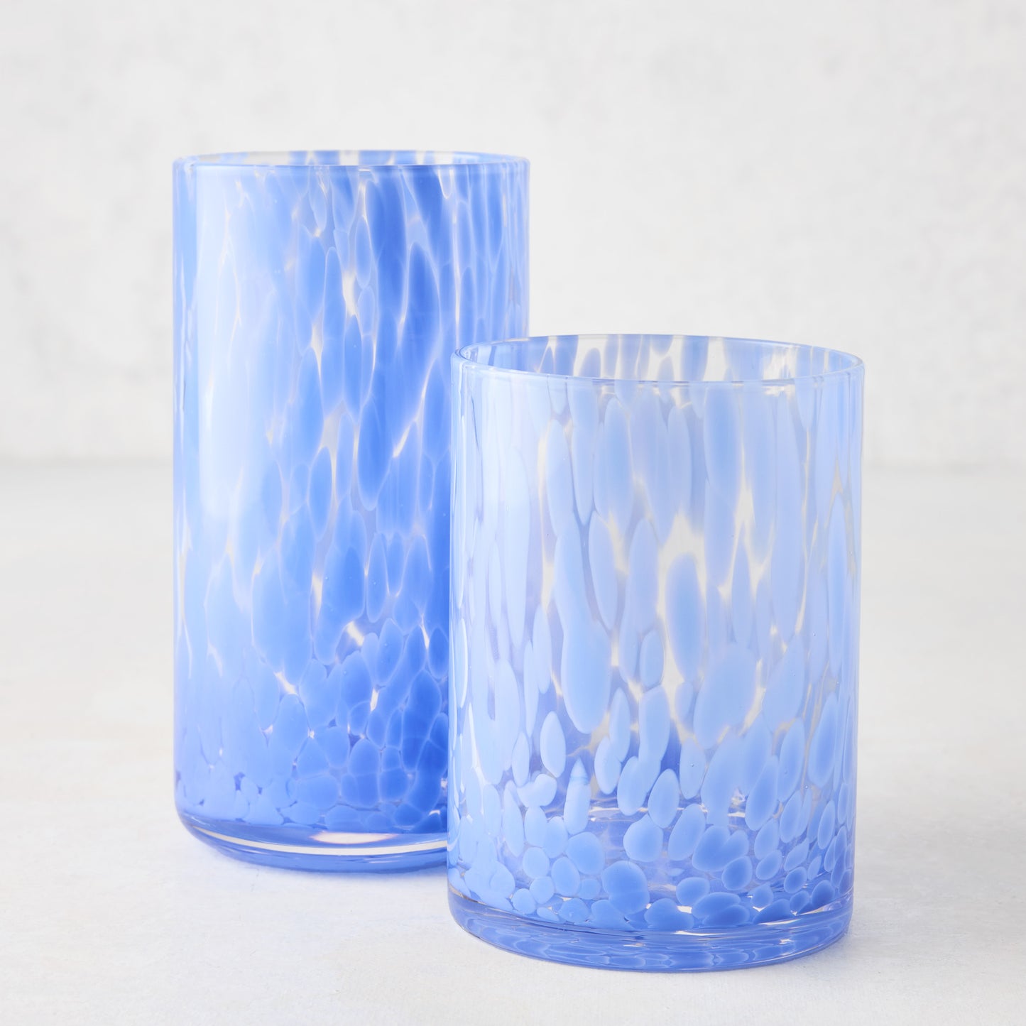 Two light blue spotted highball glasses, one tall and one shorter, on a white surface.
