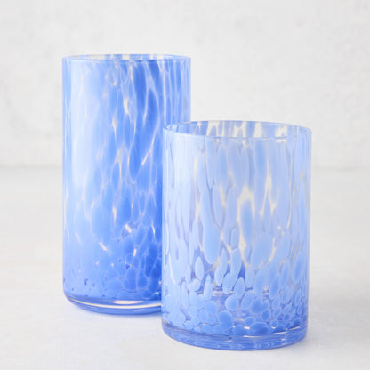 Two light blue spotted highball glasses, one tall and one shorter, on a white surface.