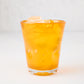 Light orange Henri mouth-blown glass, 8 oz, with ice, showing unique imperfections and air bubbles.