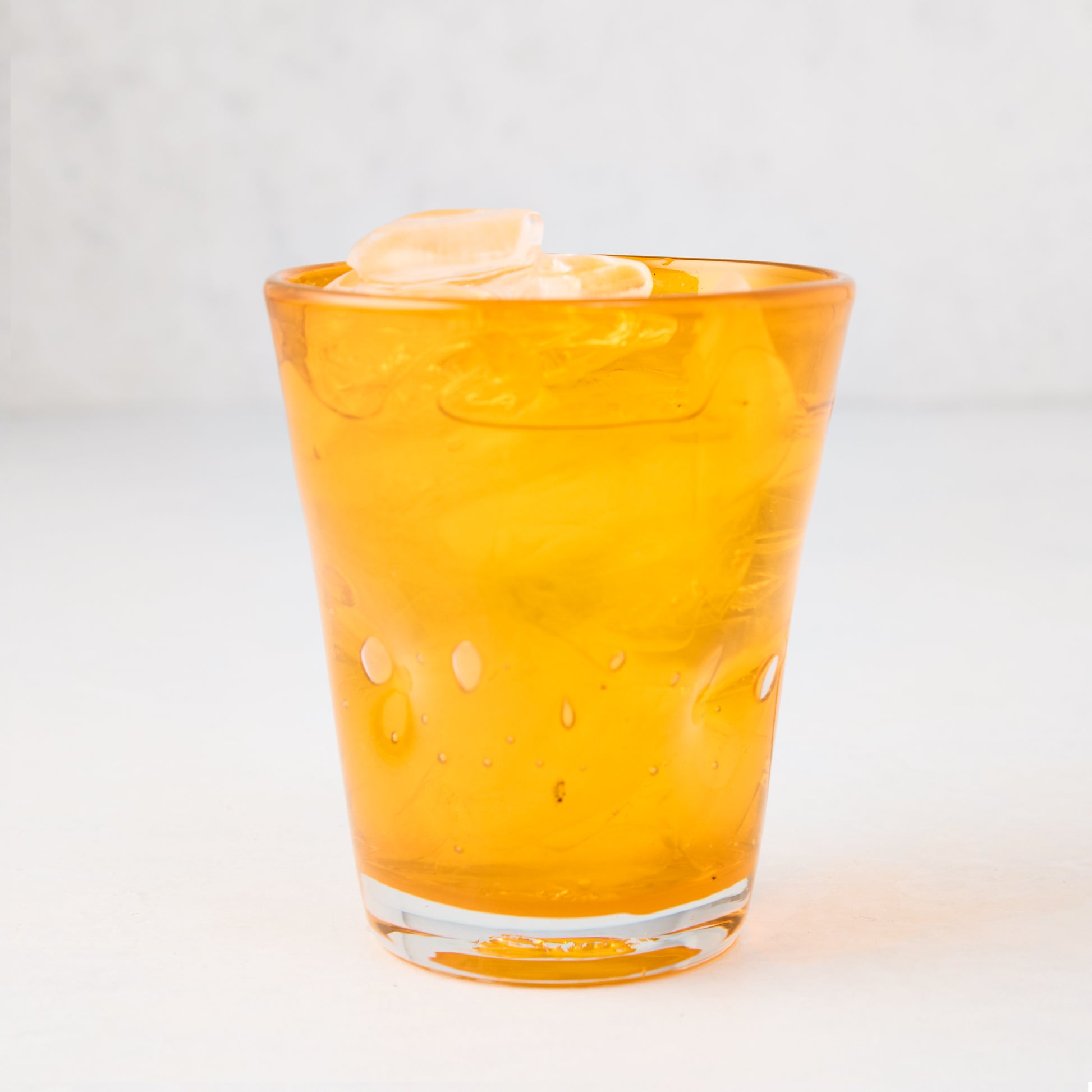 Light orange Henri mouth-blown glass, 8 oz, with ice, showing unique imperfections and air bubbles.