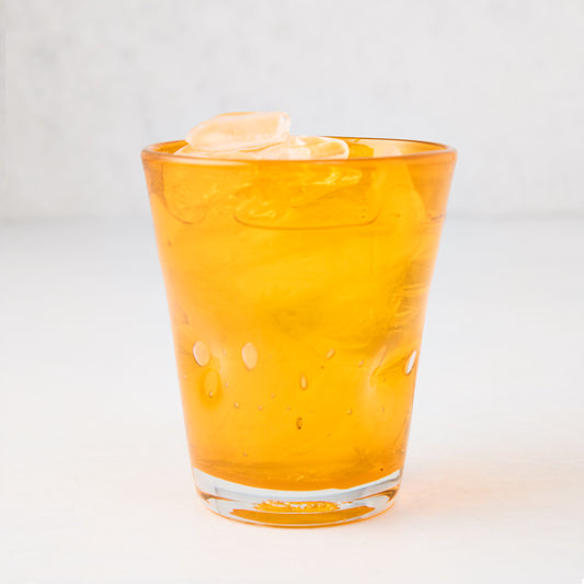 Light orange Henri mouth-blown glass, 8 oz, with ice, showing unique imperfections and air bubbles.