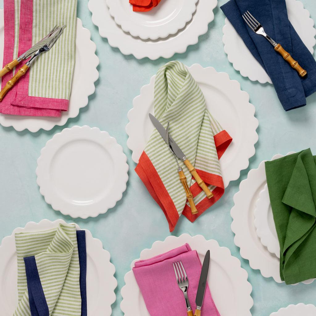 Hand-dyed Lily HG Signature linen napkins in pink, green stripe, orange, navy, and green on white scalloped plates.