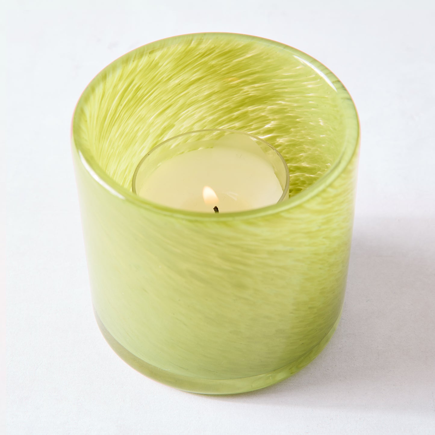 Lime green mouth-blown glass votive candle holder with a lit tealight inside.