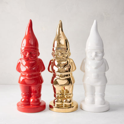 Three ceramic holiday gnomes: one red, one gold, and one white, all with pointed hats.
