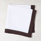 White linen napkin with a cocoa brown border, folded.