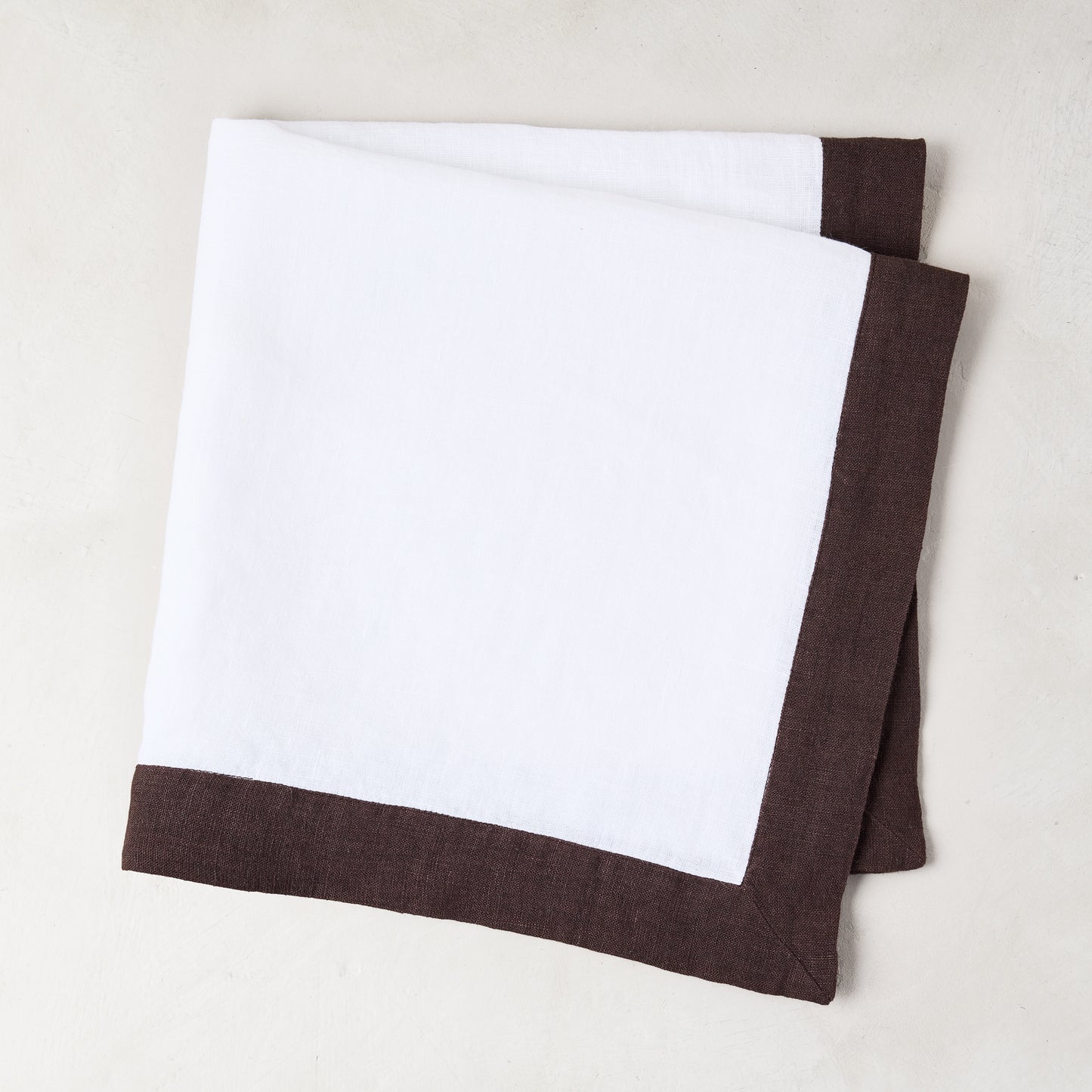 White linen napkin with a cocoa brown border, folded.
