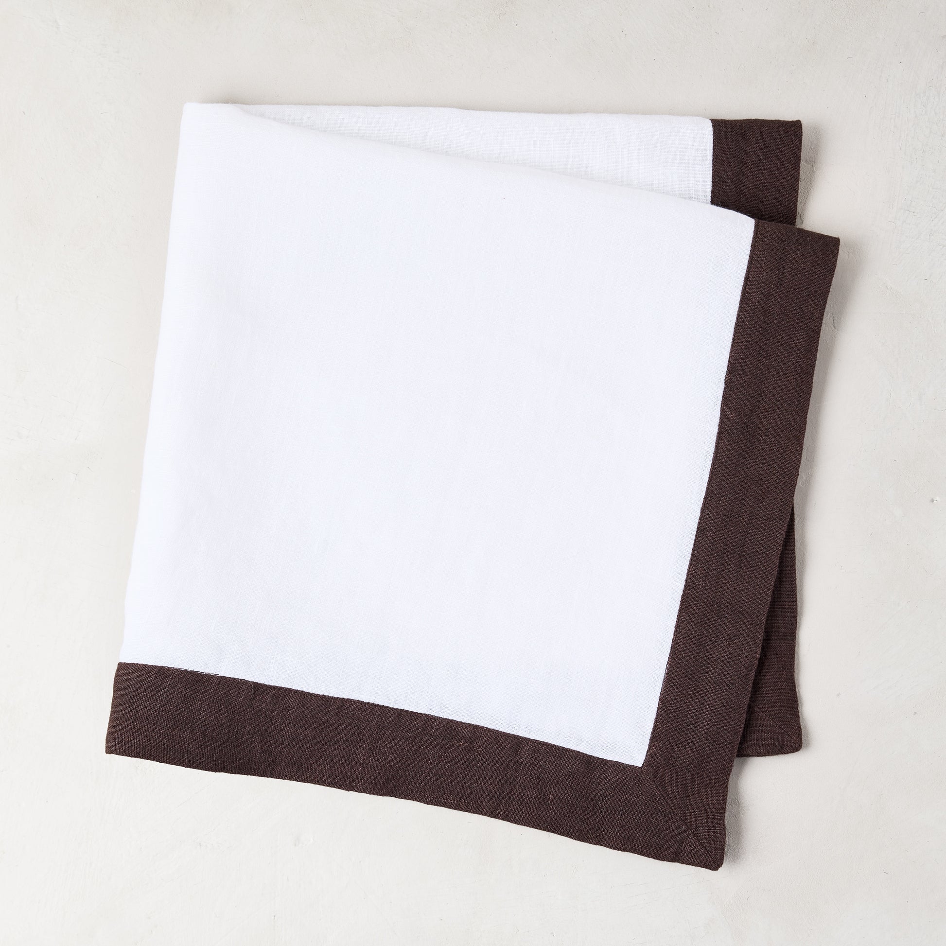 White linen napkin with a cocoa brown border, folded.