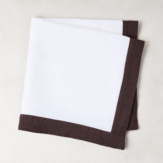 White linen napkin with a cocoa brown border, folded.