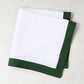 Folded white linen napkin with a fir green border.
